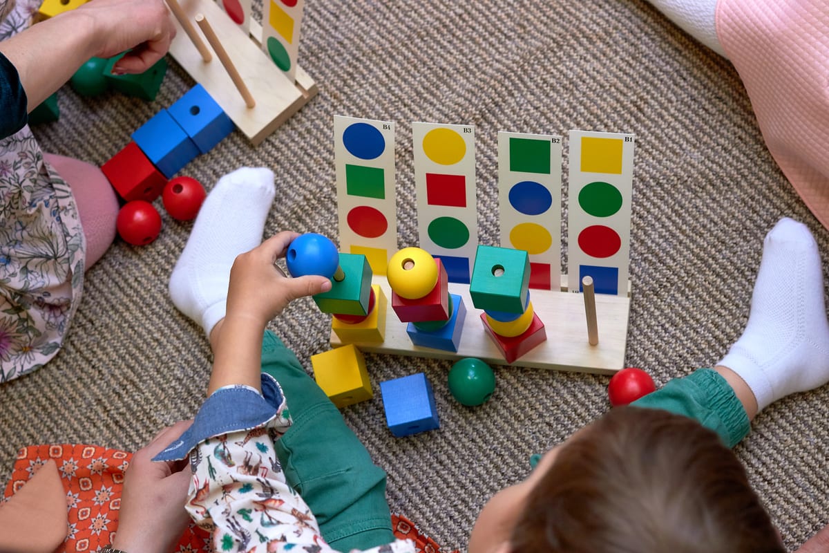 Young boy sitting on rug stacking blocks with therapist