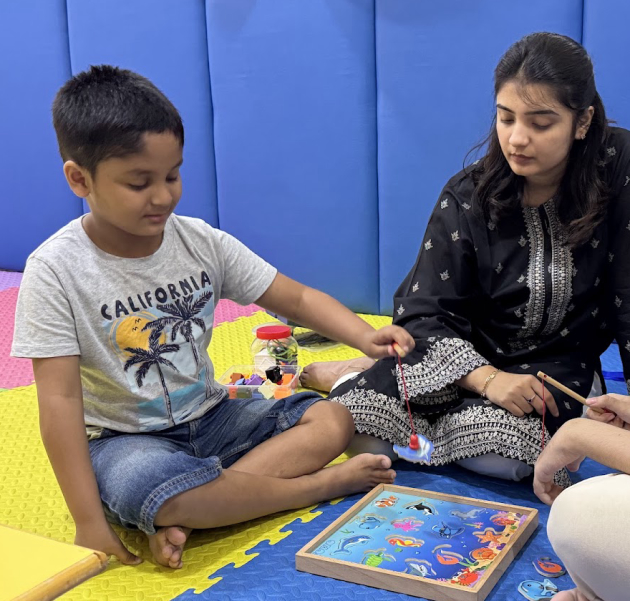 Child and therapists playing magnetic fishing game on activity mat